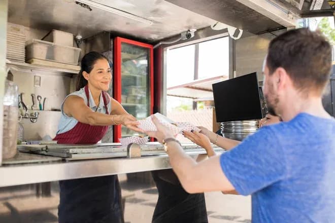 vendeuse de food truck servant un plat à un client dans un cadre extérieur convivial