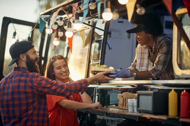 couple souriant recevant un plat d'un food truck décoré de guirlandes lumineuses