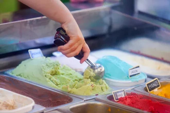 main d'une personne prenant une boule de glace verte dans un glacier avec plusieurs parfums