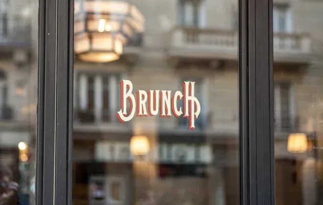 enseigne brunch sur vitrine avec reflets de lampes et façades en arrière-plan