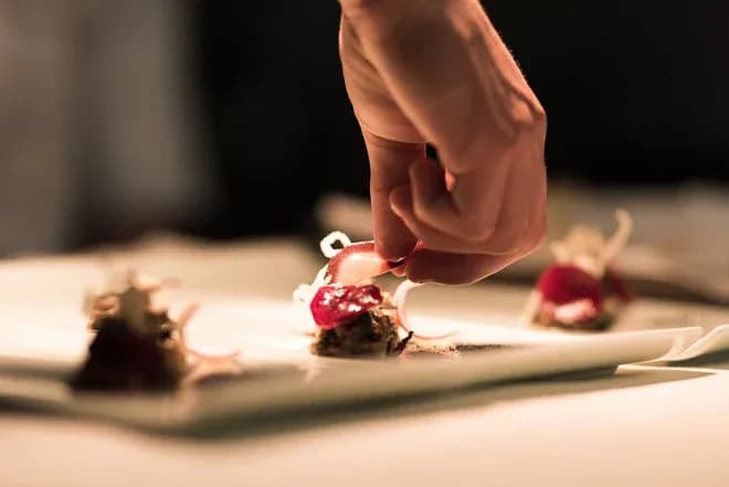 main d'un chef posant une garniture sur des amuse-bouches raffinés