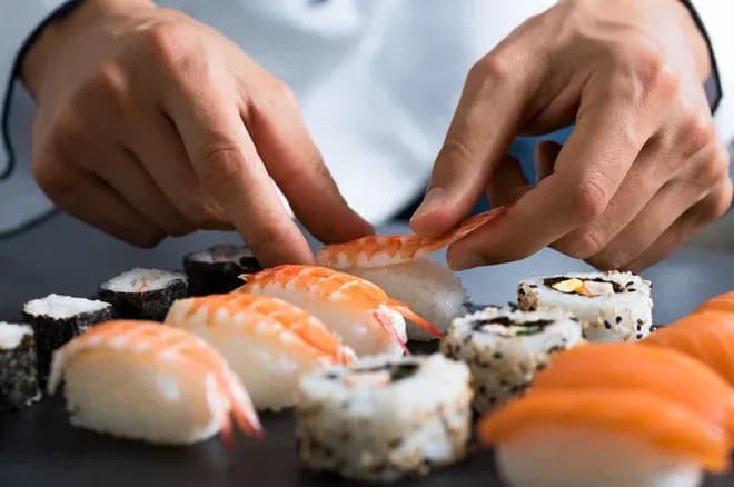 préparation de sushis avec des mains posant des crevettes sur une assiette de sushis variés