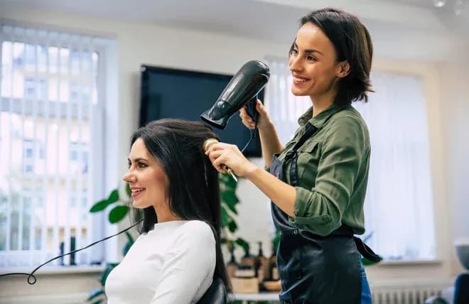 coiffeuse séchant les cheveux d'une cliente souriante au salon