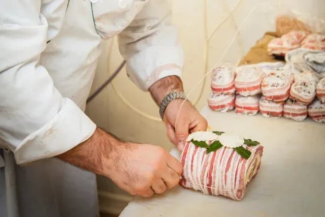mains d'artisan attachant une roulade de charcuterie bardée de lard