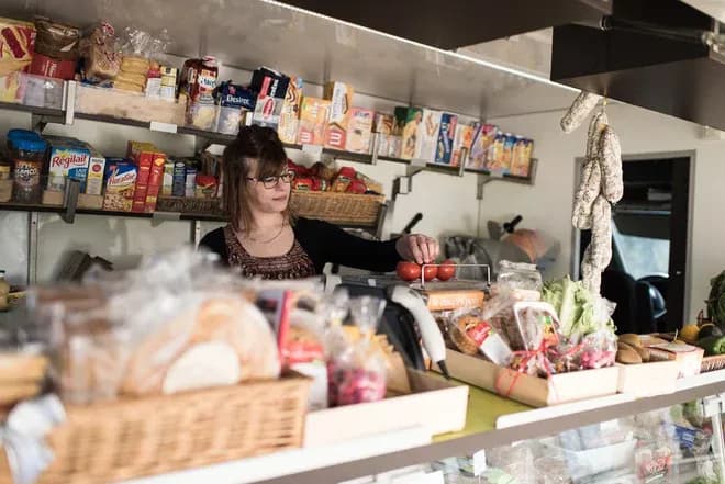 vendeuse arrangeant des tomates dans une épicerie ambulante aux étals garnis