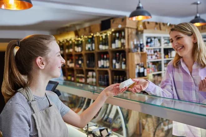 vendeuse tend un morceau de fromage à une cliente au comptoir d'une épicerie de village