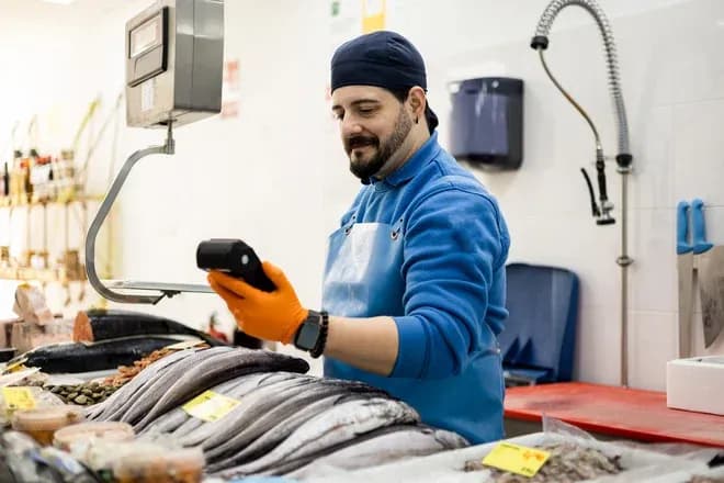 Vendeur de poisson vérifiant des informations sur un téléphone au milieu des produits de la mer