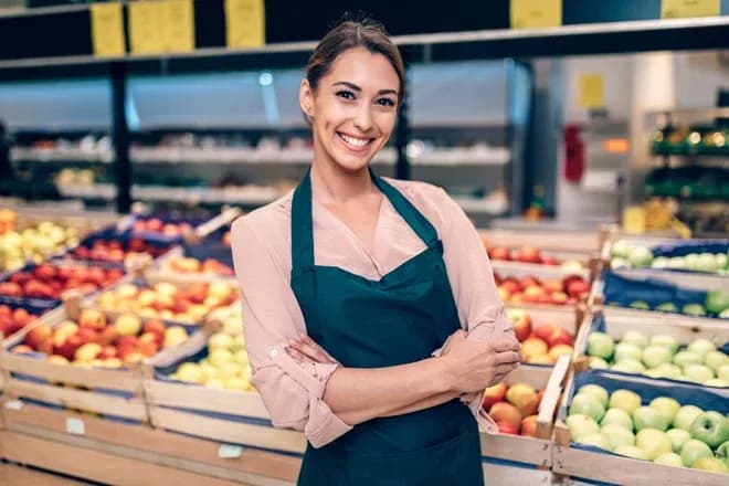 vendeuse souriante en tablier devant les fruits d'une supérette