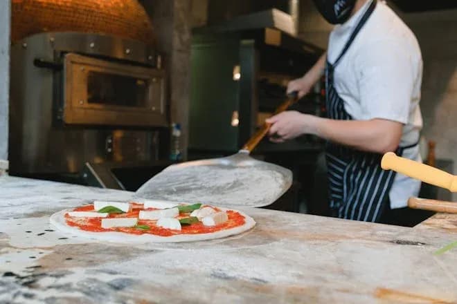 pizzaiolo préparant une pizza avec sauce tomate et mozzarella dans une pizzeria moderne