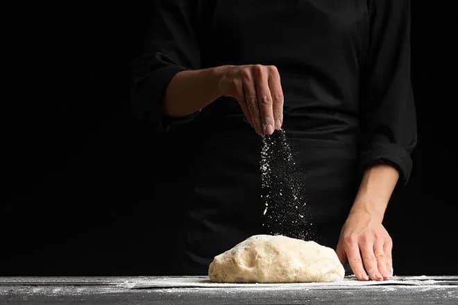 mains saupoudrant de la farine sur une boule de pâte à pain