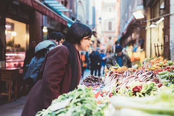 femme penchée devant étal de fruits et légumes dans une rue commerçante
