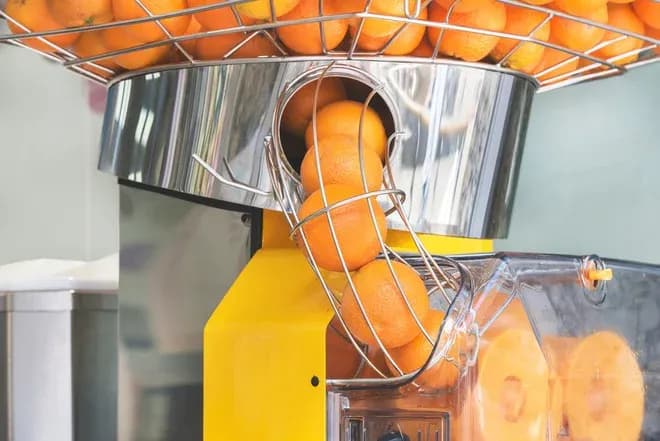 oranges acheminées dans un presse-agrume professionnel jaune et inox