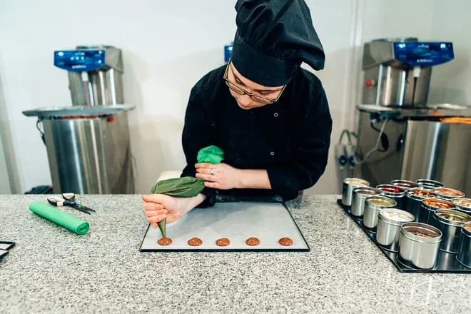 un chocolatier prépare des petits ronds de chocolat sur une plaque en cuisine professionnelle