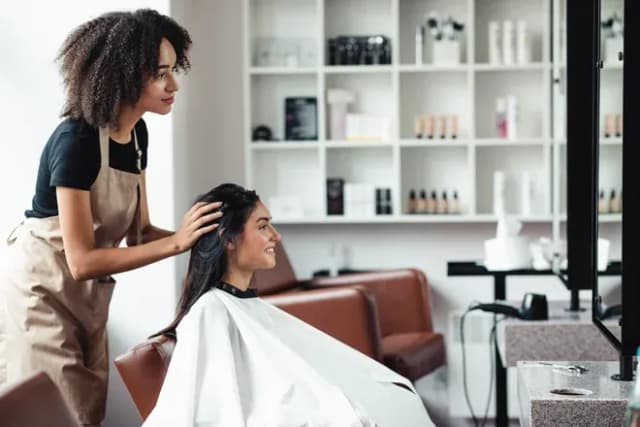 coiffeuse ajustant les cheveux d'une cliente souriante dans un salon