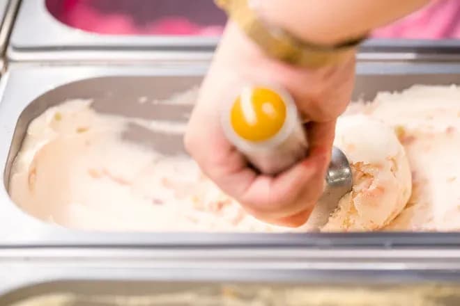 main dans un bac de glace avec une cuillère à glace pour servir une boule de crème glacée