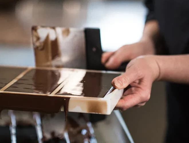 mains tenant un moule rectangulaire pendant l'écoulement du chocolat