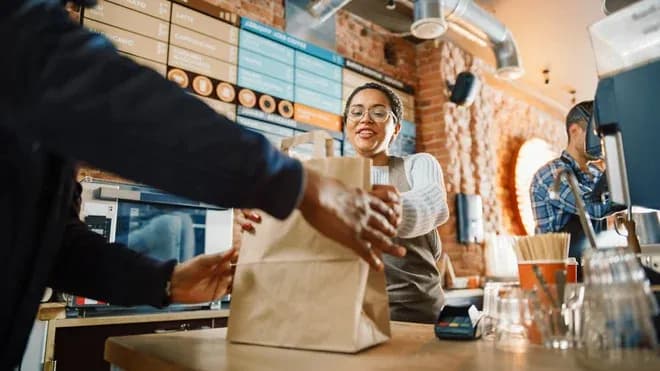 serveuse souriante tend un sac à emporter au comptoir d'un café