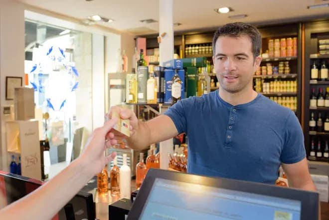 client payant par carte au comptoir d'une épicerie avec bouteilles d'alcool