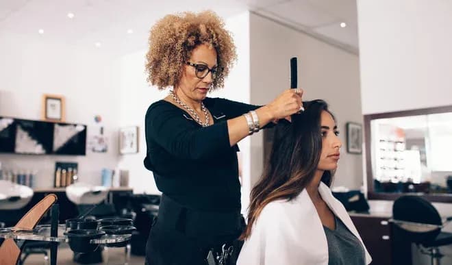 coiffeuse peigne les cheveux d'une cliente assise dans un salon