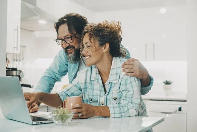 couple souriant ensemble devant un ordinateur portable dans une cuisine moderne