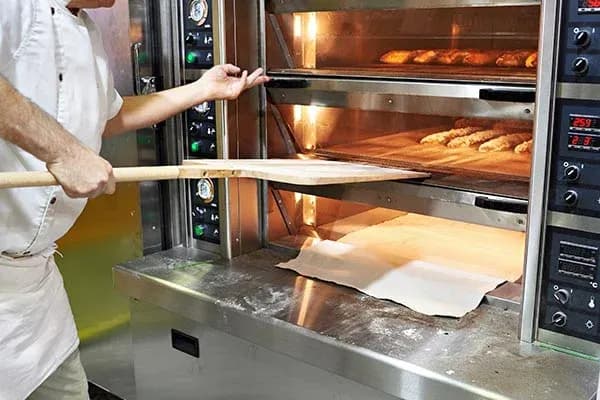 boulanger sortant des pains du four avec une pelle en bois dans une boulangerie professionnelle