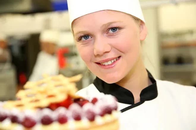 apprentie pâtissière souriante tenant une tarte aux fruits rouges