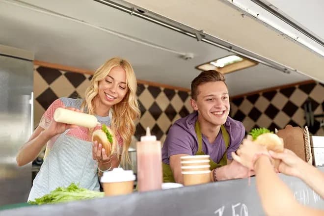 vendeurs souriants dans un food truck préparant un burger pour un client
