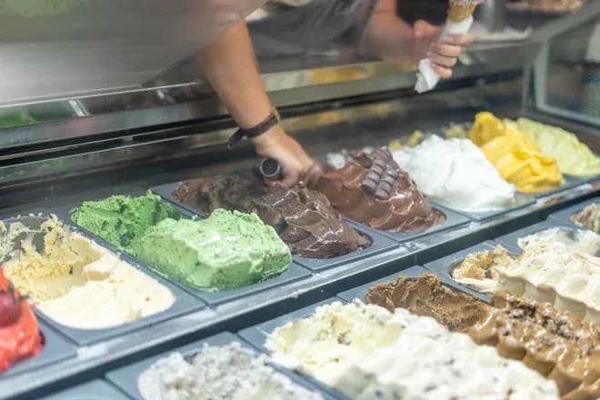 main sert un cornet de glace chocolat devant une vitrine de parfums variés