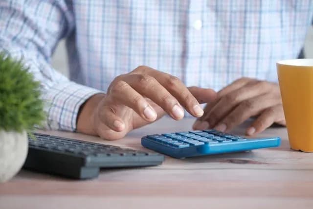 mains utilisant une calculatrice bleue sur un bureau avec clavier et tasse