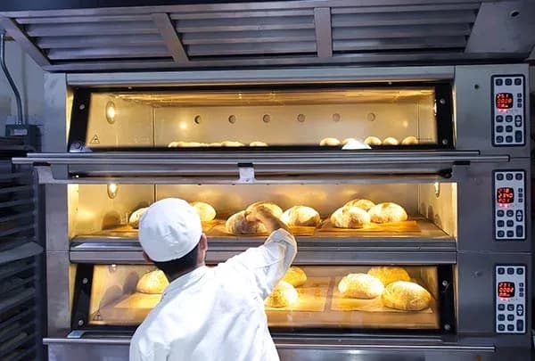 un boulanger sort des pains d'un four à plusieurs niveaux éclairé à l'intérieur