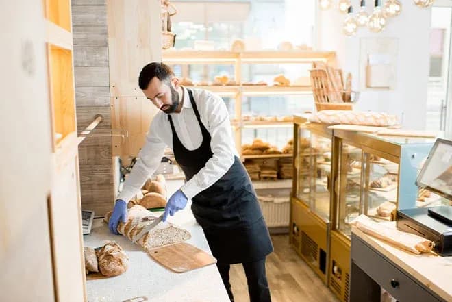 Vendeur en boulangerie coupant du pain sur un plan de travail en marbre