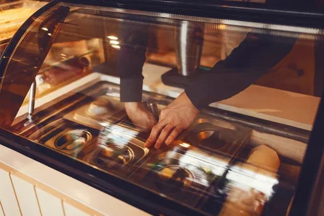 main tenant une vitrine de glacier avec des bacs de glace et un shaker à côté