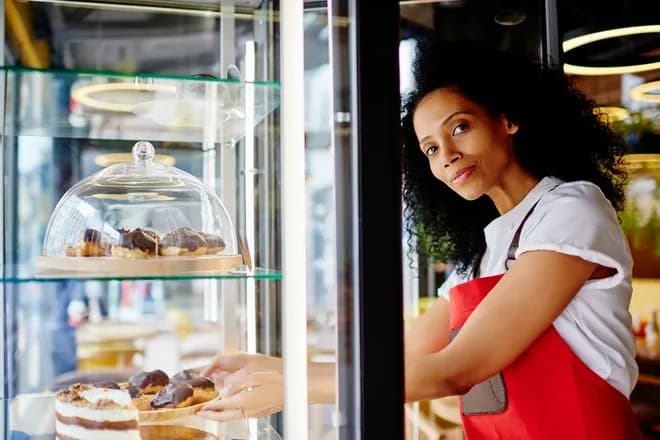 femme souriante dans une vitrine de pâtisserie avec des gâteaux et des pâtisseries