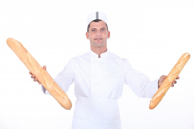 Boulanger qui tient une baguette dans chaque main.