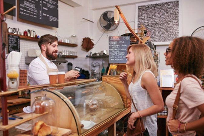 Commerçant entrain d'encaisser des clientes dans son café qui payent par carte bancaire.