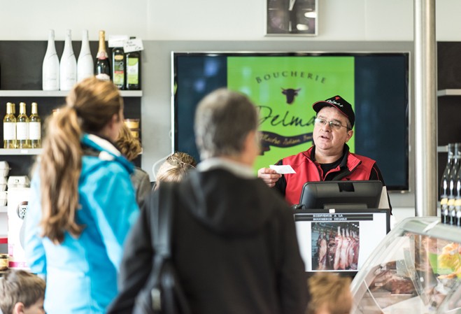 Un boucher au comptoir de sa boutique recevant des clients