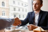 Homme en costume bleu et chemise blanche serra la main d'une autre personne dans un café