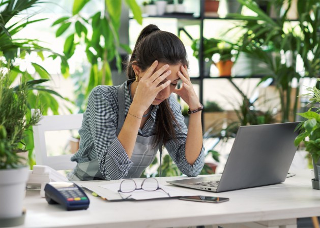 Femme qui est épuisée, penchée sur son bureau la tête dans ses mains.