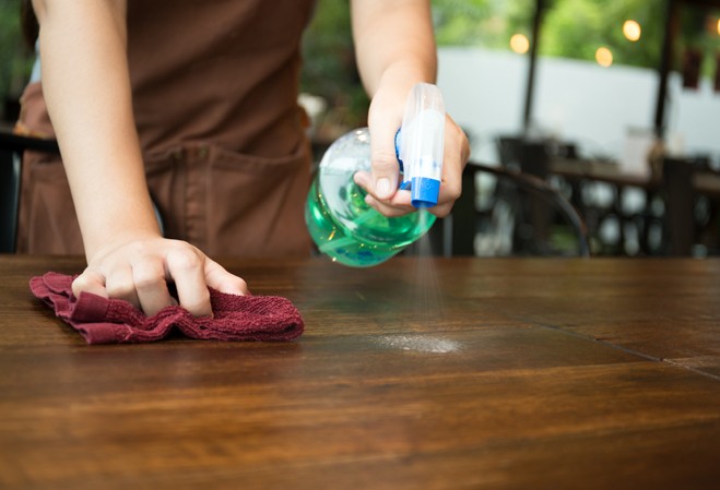 Personne nettoyant une table de restaurant avec un produit nettoyant