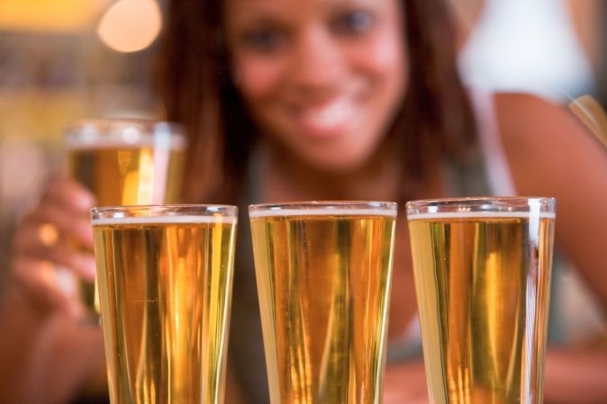Gros plan sur 3 verres de bière dans un bar ou un pub avec en arrière plan une femme souriante tenant une autre bière à la main