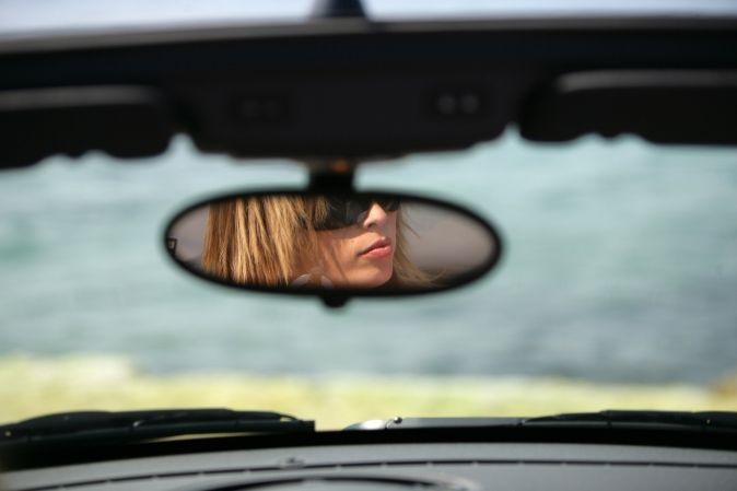 Reflet d'une conductrice dans son rétroviseur central, entrain de conduire et portant des lunettes de soleil