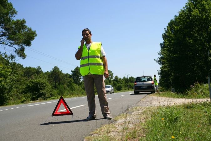 Automobiliste au téléphone portant un gilet jaune à côté d'un triangle de pré-signalisation