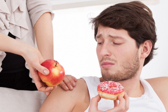 Homme en train de manger une pâtisserie et regardant une pomme tendue par une main