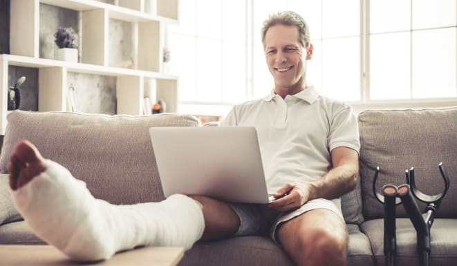 Homme avec un plâtre à la jambe entrain de travailler sur l'ordinateur