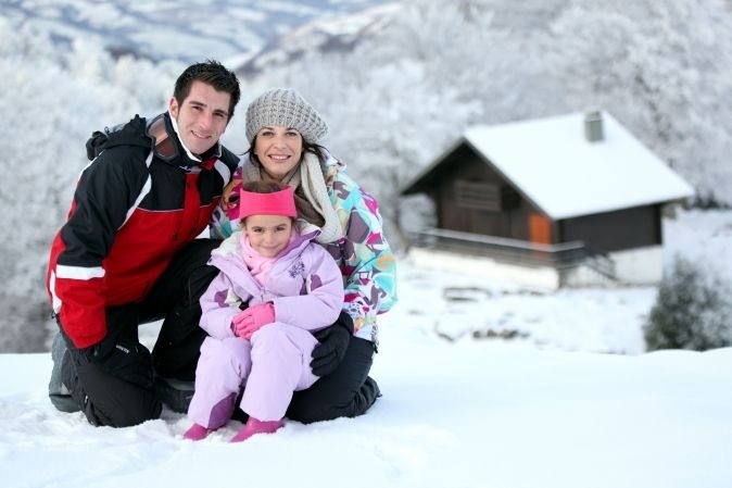 Famille aux sports d'hiver qui pose devant un paysage enneigé avec au fond un chalet en bois