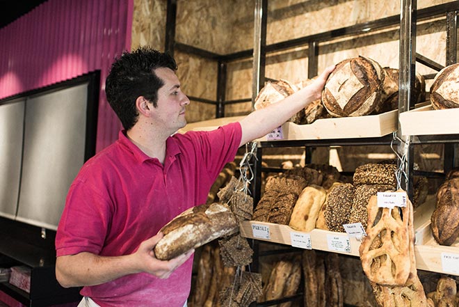 Boulanger entrain de mettre du pain en rayon dans sa boulangerie