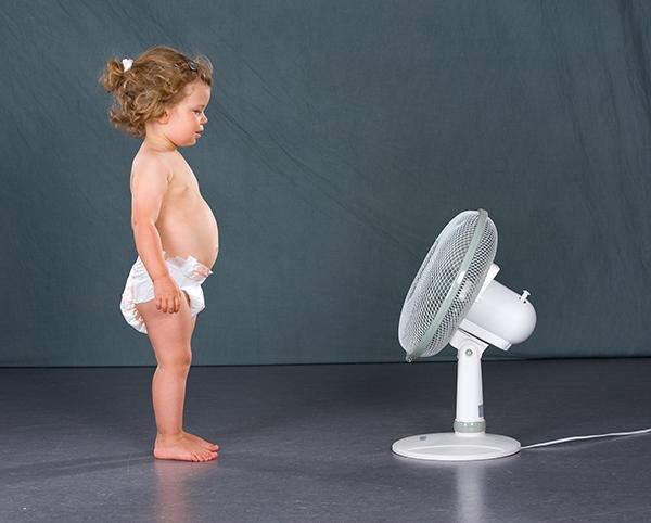 Petite fille en couche culotte debout devant un ventilateur en marche