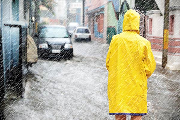 Femme en k-way jaune devant une route inondée, et sous une pluie diluvienne