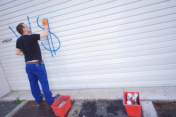 Commerçant entrain de nettoyer un graffiti sur le rideau métallique de son commerce