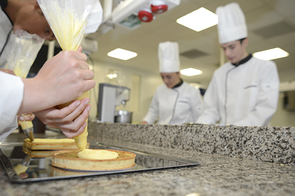 Deux pâtissiers déposent de la crème sur leur préparation de gâteau